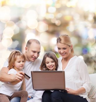 family, holidays, shopping, technology and people - happy family with laptop computer and credit card over lights background