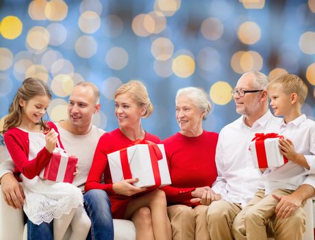 family, holidays, generation, christmas and people concept - smiling family with gift boxes sitting on couch over blue lights background