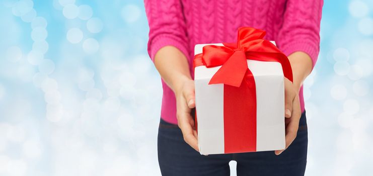 christmas, holidays and people concept - close up of woman in pink sweater holding gift box over blue lights background