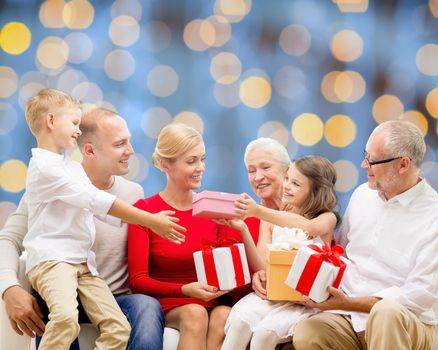 family, holidays, generation, christmas and people concept - smiling family with gift boxes sitting on couch over blue lights background