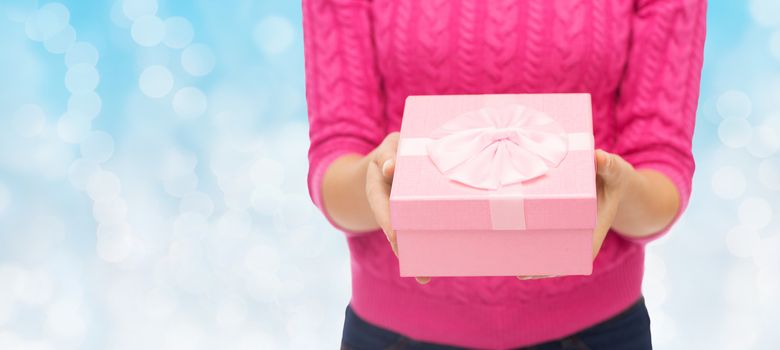 christmas, holidays and people concept - close up of woman in pink sweater holding gift box over blue lights background