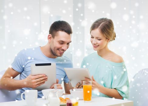 food, family, people and technology concept - smiling couple with tablet pc computers reading news and having breakfast at home