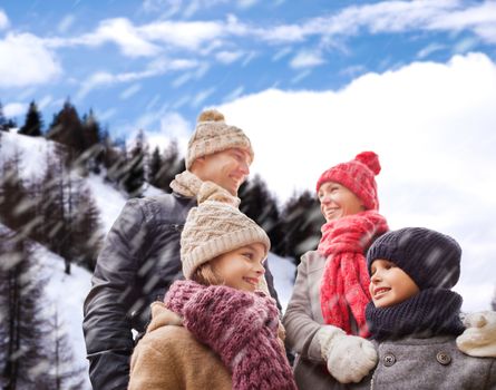 family, childhood, season and people concept - happy family in winter clothes over snowy mountains background