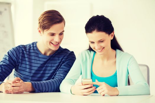 education, relationships and technology concept - two smiling students with smartphone at school