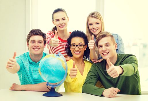 education, travel and geography concept - five smiling student with earth globe at school showing thumbs up