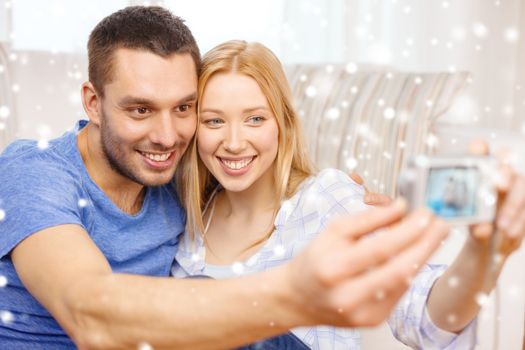 love, family, technology and happiness concept - smiling couple taking self portrait picture with digital camera at home