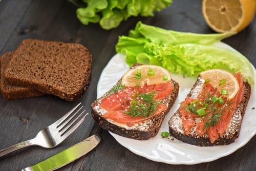 Homemade sandwich with salmon and rye bread , butter lemon, and lettuce for breakfast