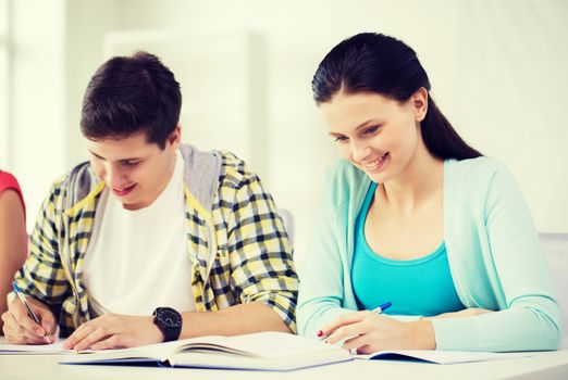 education and school concept - two smiling students with textbooks and books at school