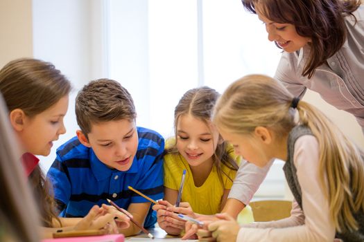 education, elementary school, learning and people concept - teacher helping school kids writing test in classroom