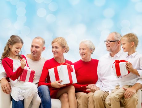 family, holidays, generation, christmas and people concept - smiling family with gift boxes sitting on couch over blue lights background