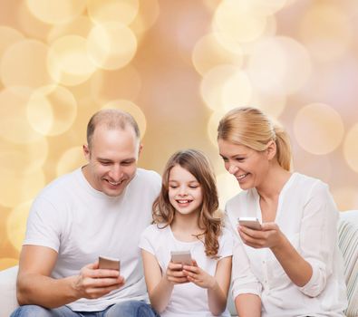 family, holidays, technology and people - smiling mother, father and little girl with smartphones over beige lights background