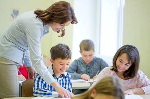 education, elementary school, learning and people concept - teacher helping school kids writing test in classroom