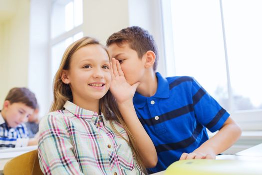 education, elementary school, learning and people concept - smiling schoolboy whispering secret to classmate ear in classroom