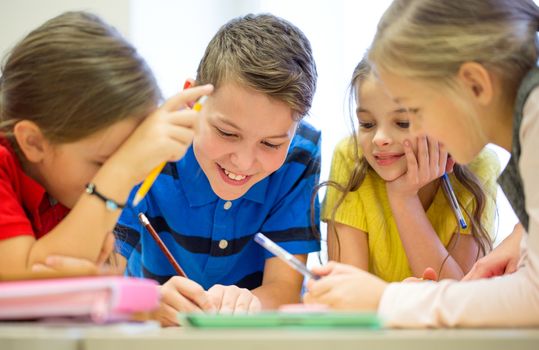 education, elementary school, learning and people concept - group of school kids with pens and papers writing in classroom