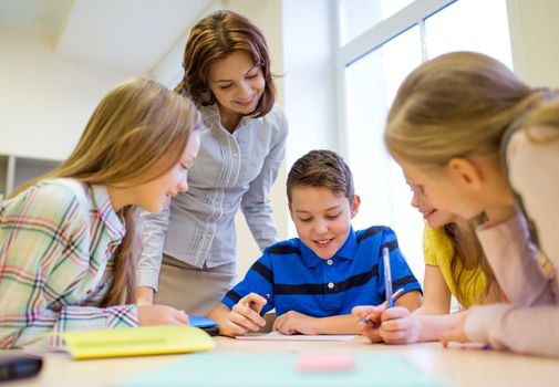 education, elementary school, learning and people concept - teacher helping school kids writing test in classroom