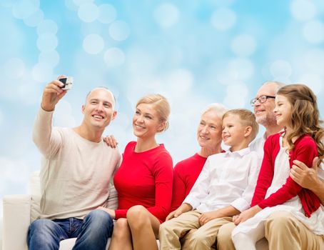 family, holidays, generation, christmas and people concept - smiling family with camera taking selfie and sitting on couch over blue lights background