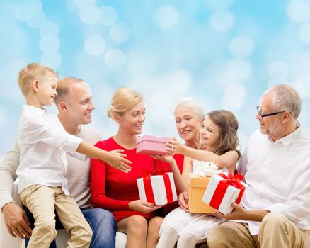 family, holidays, generation, christmas and people concept - smiling family with gift boxes sitting on couch over blue lights background