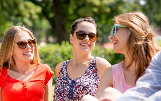 friendship, leisure, summer and people concept - group of smiling friends outdoors sitting on grass in park