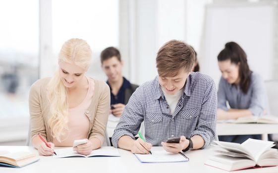 education and technology concept - group of students looking into smartphone at school