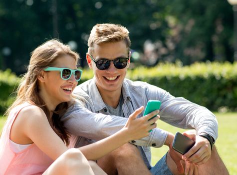 friendship, leisure, summer, technology and people concept - group of smiling friends with smartphone sitting on grass in park