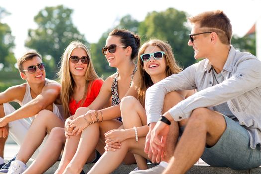 friendship, leisure, summer and people concept - group of smiling friends sitting on city street