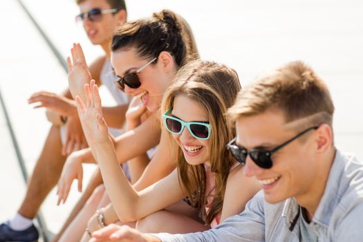 friendship, leisure, summer, gesture and people concept - group of laughing friends sitting on city square