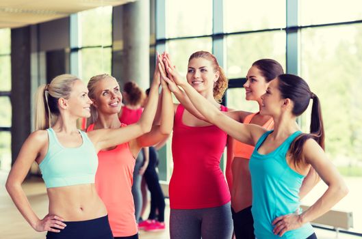 fitness, sport, friendship and lifestyle concept - group of women making high five gesture in gym