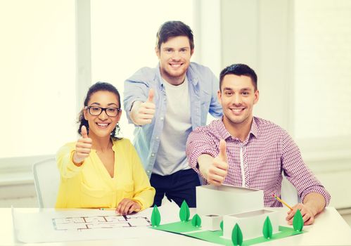 startup, education, architecture and office concept - smiling architects with house model and blueprint in office showing thumbs up