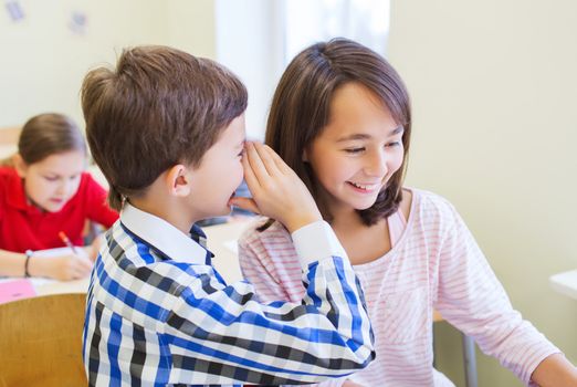 education, elementary school, learning and people concept - smiling schoolboy whispering secret to classmate ear in classroom