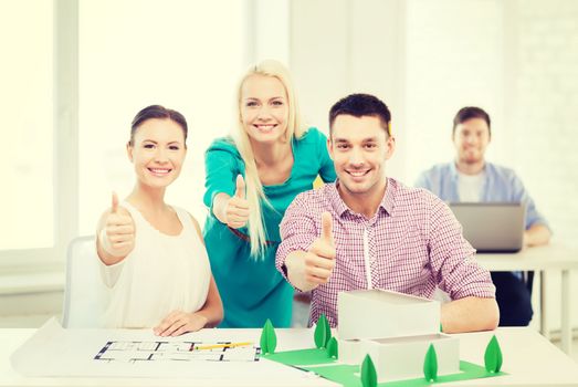 startup, education, architecture and office concept - smiling architects with house model and blueprint in office showing thumbs up