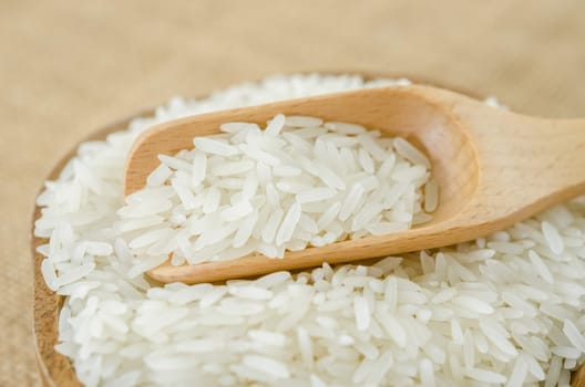 Raw rice in wooden bowl with wooden spoon on sack background.