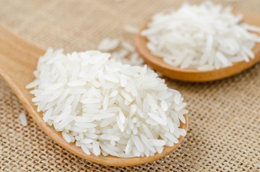 Raw rice in wooden spoon on sack background.
