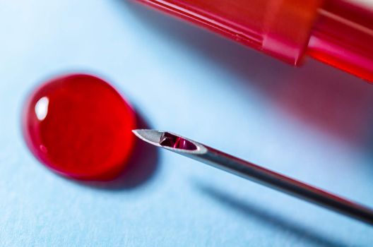Extracted blood in syringe with hypodermic needle, blood drops in laboratory.