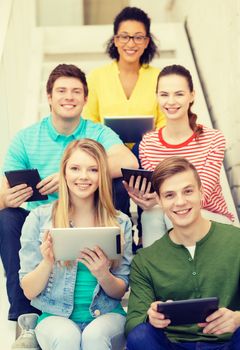 education and technology concept - smiling students with tablet pc computer sitting on staircase