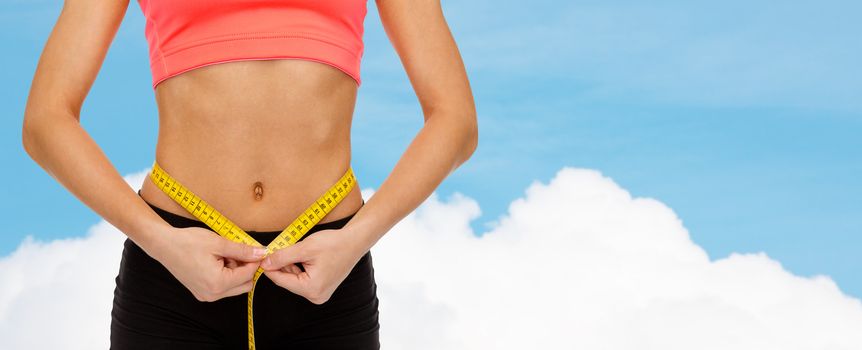 diet, sport, fitness and heath concept - close up of female hands measuring waist with measuring tape