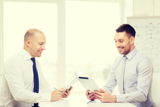 business, technology and office concept - two smiling businessmen with tablet pc computers and files in office