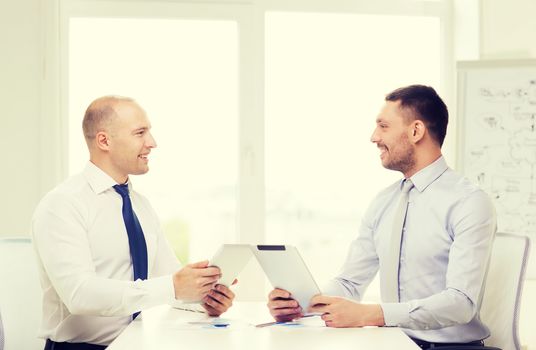 business, technology and office concept - two smiling businessmen with tablet pc computers and files in office