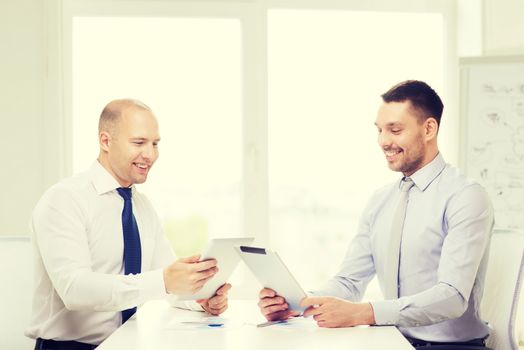 business, technology and office concept - two smiling businessmen with tablet pc computers and files in office