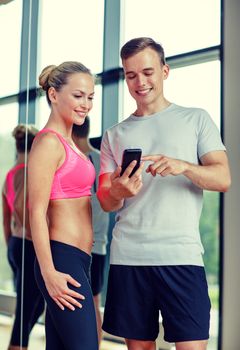 fitness, sport, exercising, technology and diet concept - smiling young woman and personal trainer with smartphone in gym