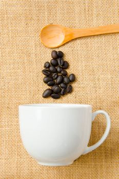 Seed coffee, wooden spoon and a cup of coffee on a background sacks.