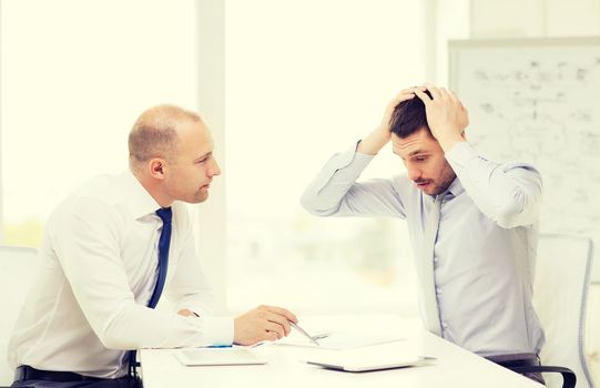 business, technology and office concept - two serious businessmen with tablet pc computers and files in office