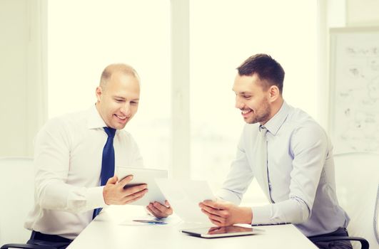 business, technology and office concept - two smiling businessmen with tablet pc computers and files in office