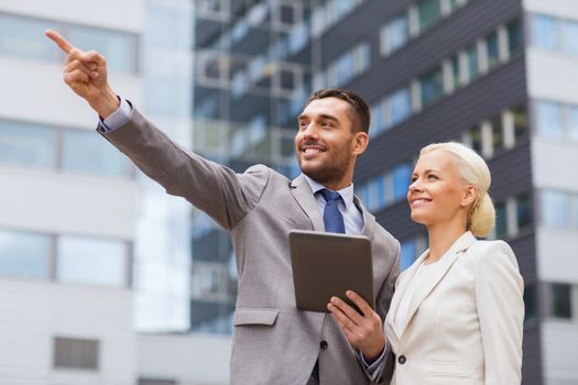 business, partnership, technology and people concept - smiling businessman and businesswoman with tablet pc computer over office building