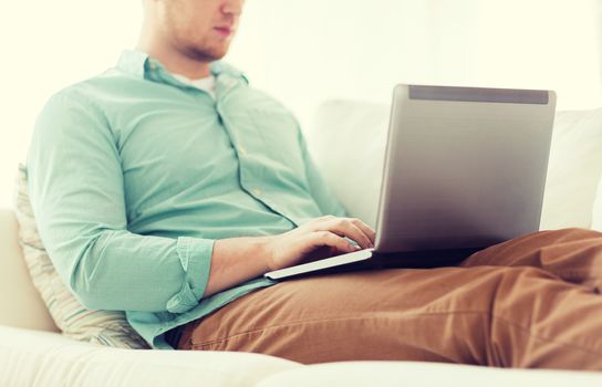 technology, home and lifestyle concept - close up of man working with laptop computer and sitting on sofa at home