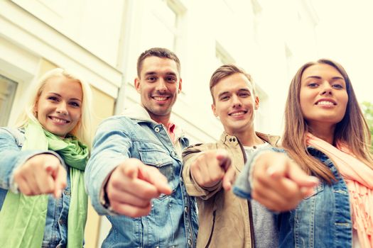 travel, vacation and friendship concept - group of smiling friends in city pointing finger at you