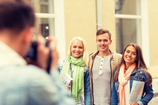 travel, vacation, technology and friendship concept - guy picturing group of friends with map and city guide in city