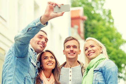 travel, vacation, technology and friendship concept - group of smiling friends making selfie with smartphone camera outdoors