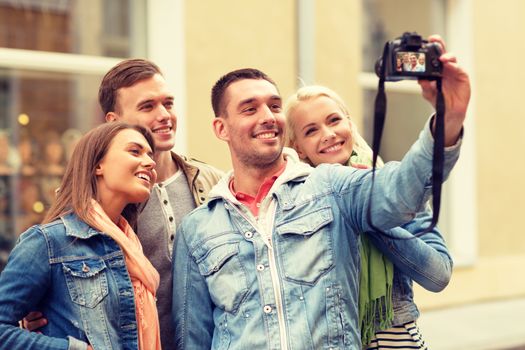 travel, vacation, technology and friendship concept - group of smiling friends making selfie with digital camera outdoors