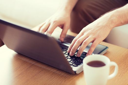 technology, home, drinks and lifestyle concept - close up of man with laptop and cup of coffee at home