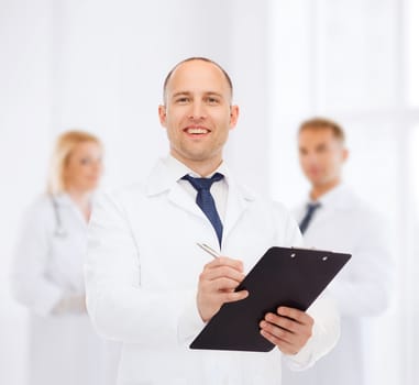 medicine, profession, teamwork and healthcare concept - smiling male doctor with clipboard writing prescription over group of medics